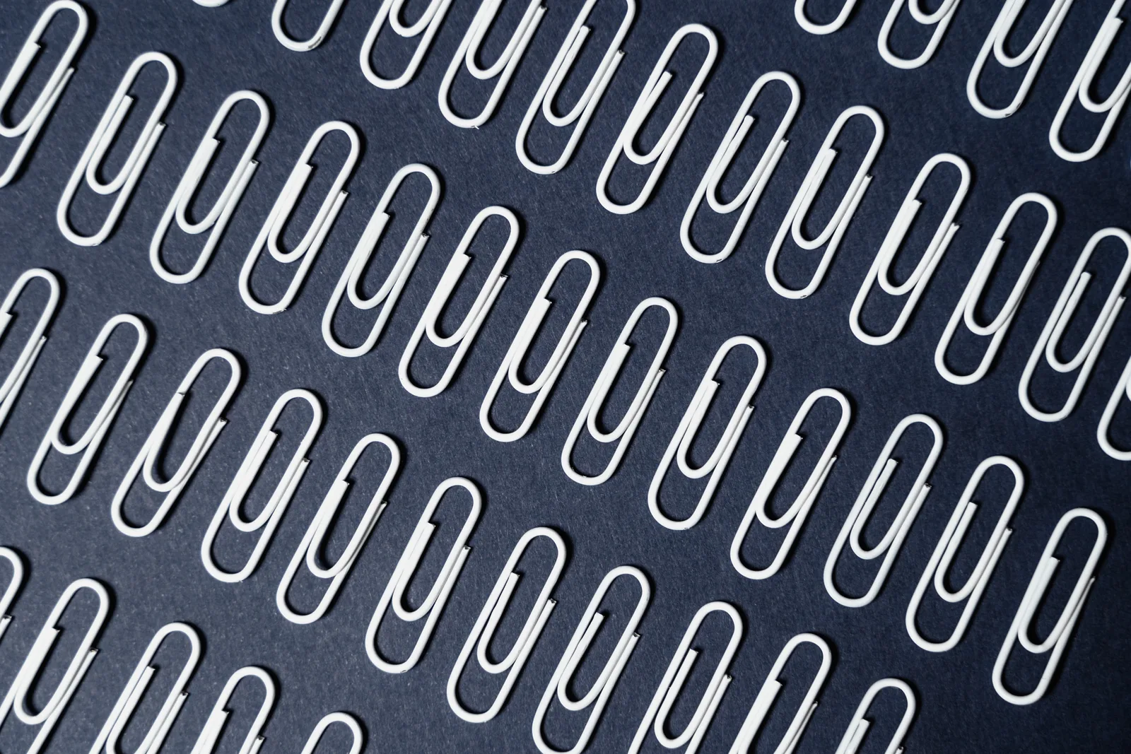 Close-up of neatly arranged paper clips on a dark surface creating a repeating pattern.