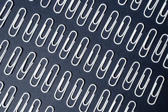 Close-up of neatly arranged paper clips on a dark surface creating a repeating pattern. Detecting repeated exposure across line items