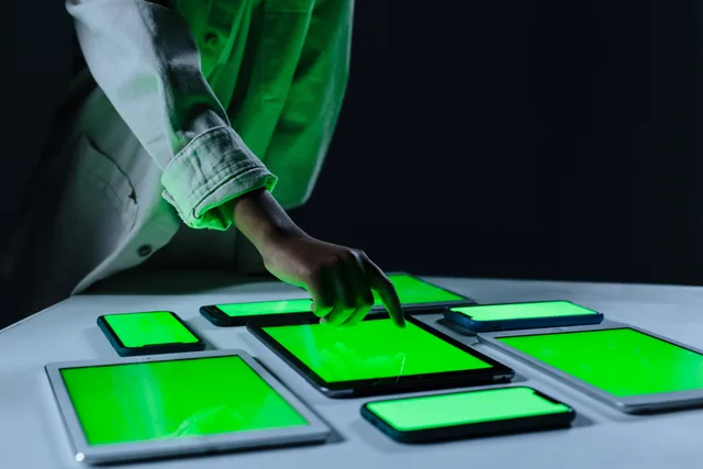 Hand interacting with multiple digital tablets on a green screen setup indoors. Frequency management in programmatic campaigns